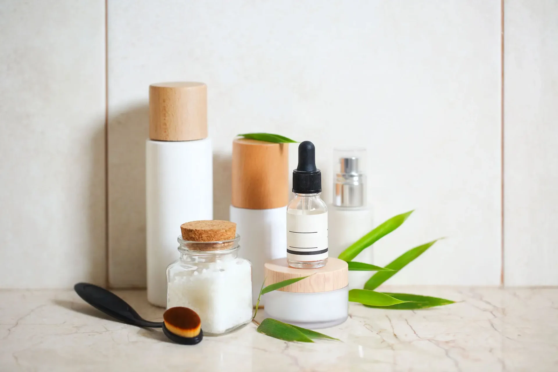 Skincare products with green leaves on marble.