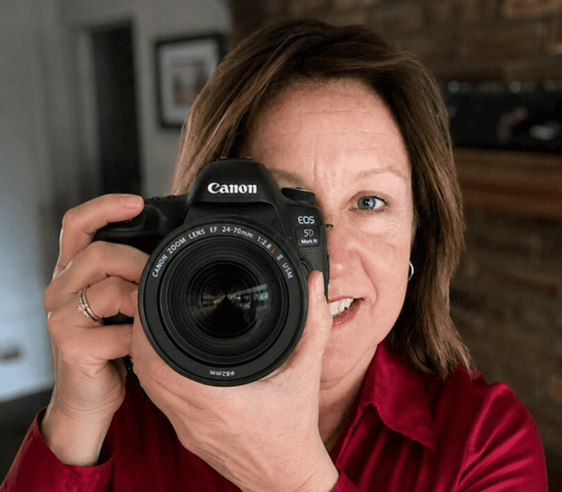 Person holding Canon camera, smiling indoors.