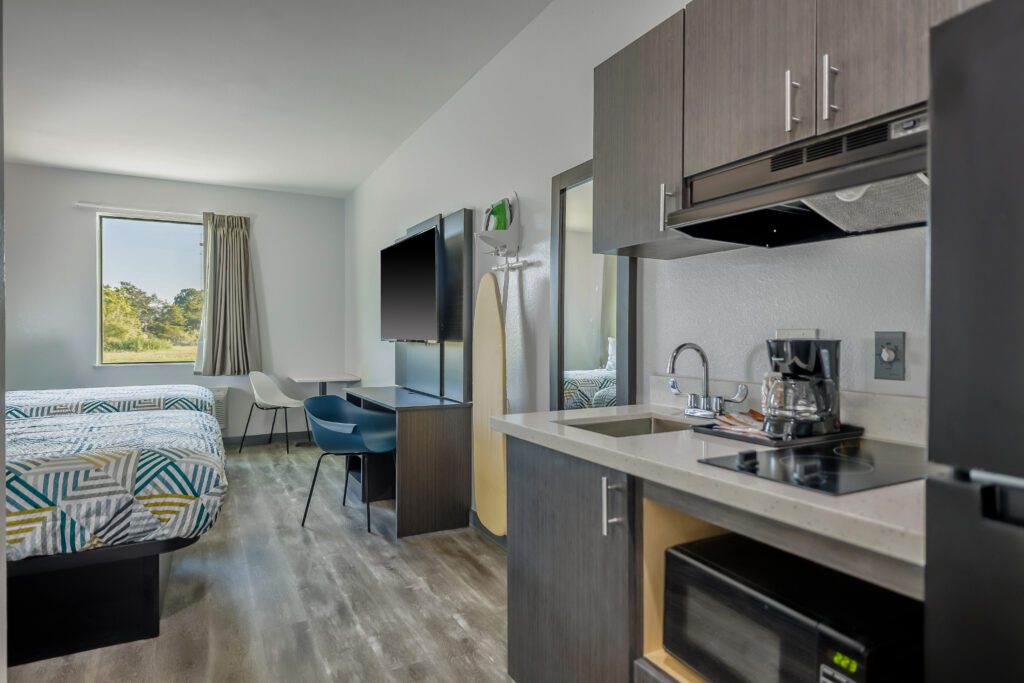 Modern hotel room with kitchenette and bed.